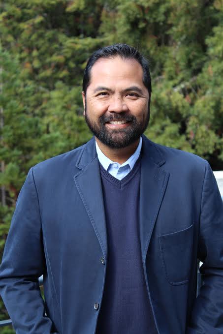 headshot of glenn gumin in blue blazer with greenery in background